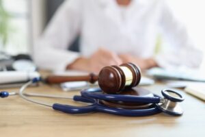 A stethoscope and gavel on a desk, with a doctor or lawyer working in the background.